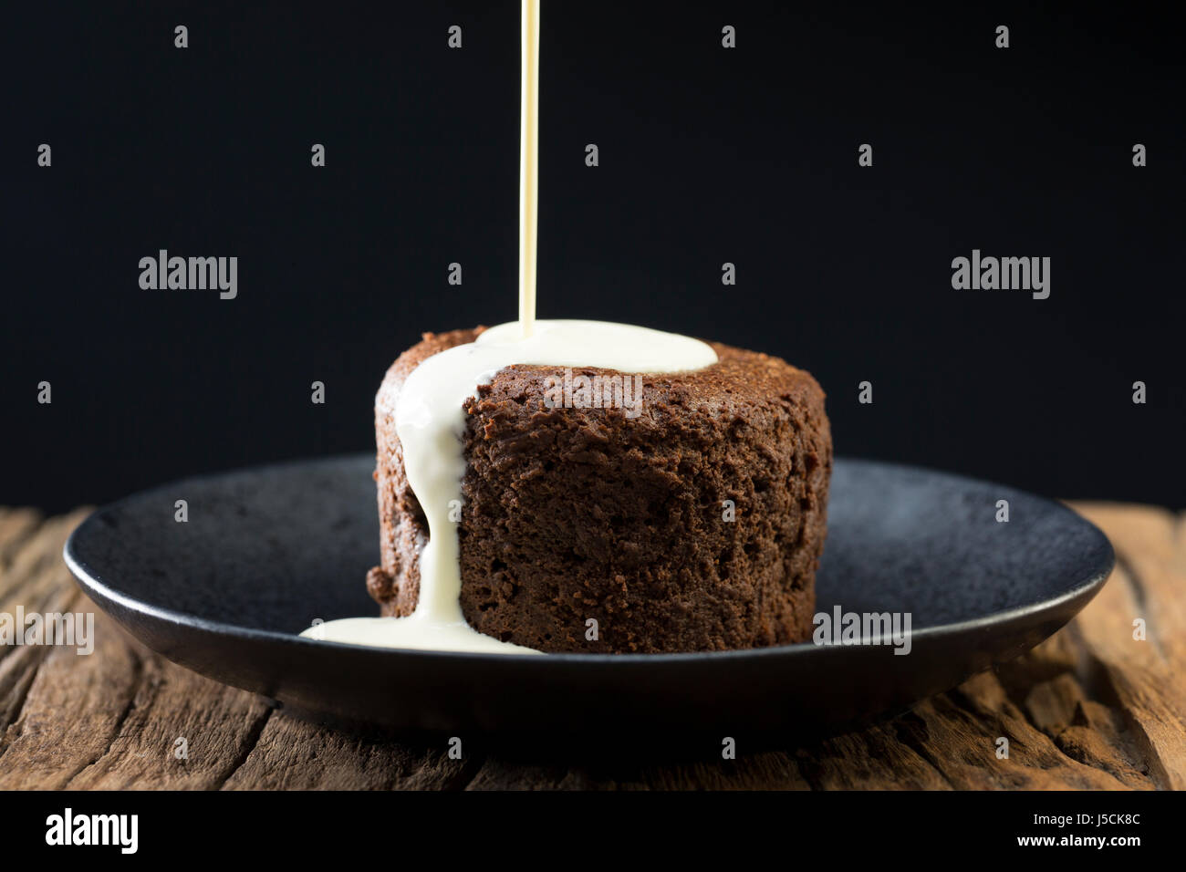 Panna fresca che viene colato su un cioccolato torta di lava. Budino di cioccolato seduta su una tavola in legno rustico. Foto Stock