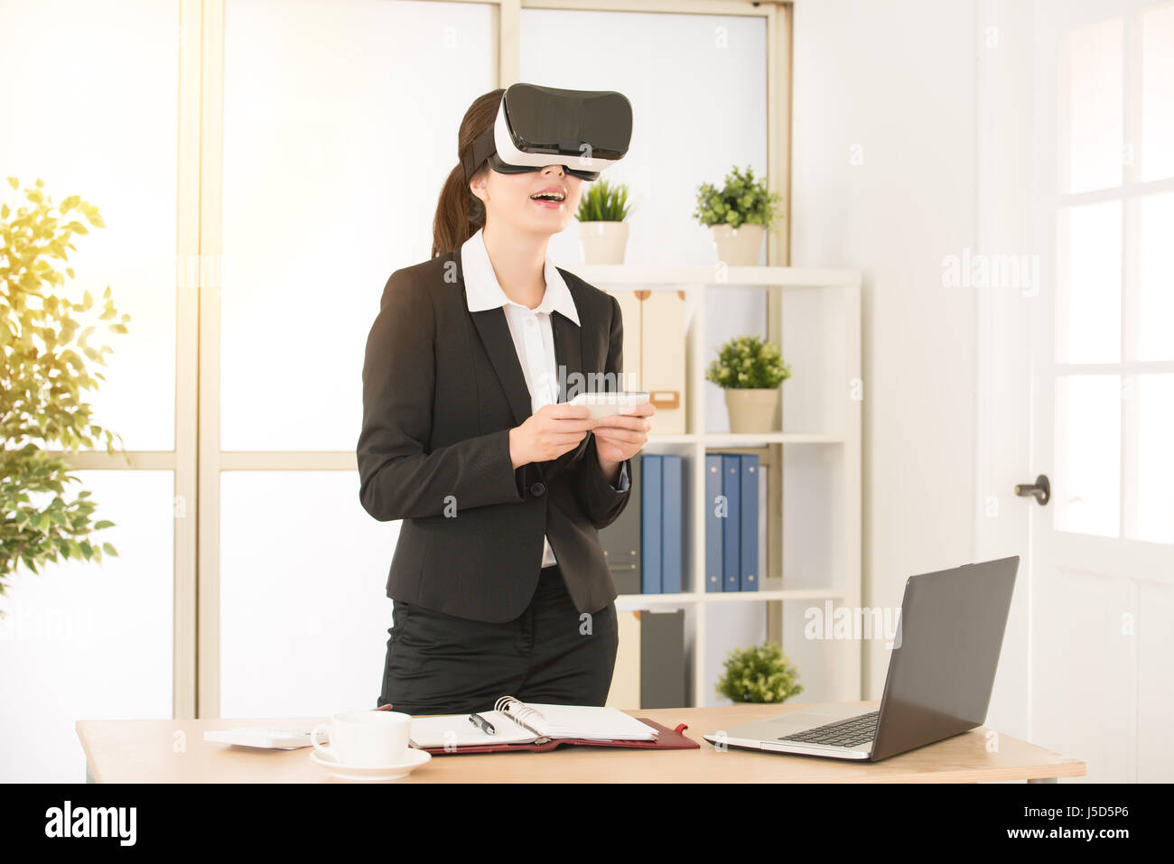 Razza mista cinese asiatica giovane donna felice di giocare con i videogiochi occhiali per realtà virtuale nella luminosa workplace allegro per divertirti con le nuove tendenze tec Foto Stock