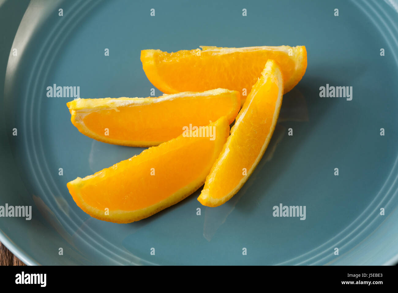 Quattro spicchi d'arancia seduti in una ciotola blu. Foto Stock