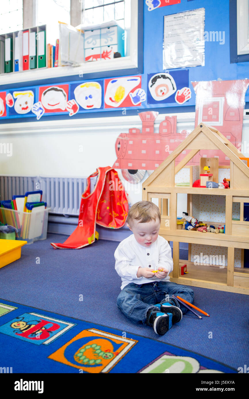 La sindrome di Down ragazzo giocando con matite colorate nel suo vivaio in aula. Foto Stock