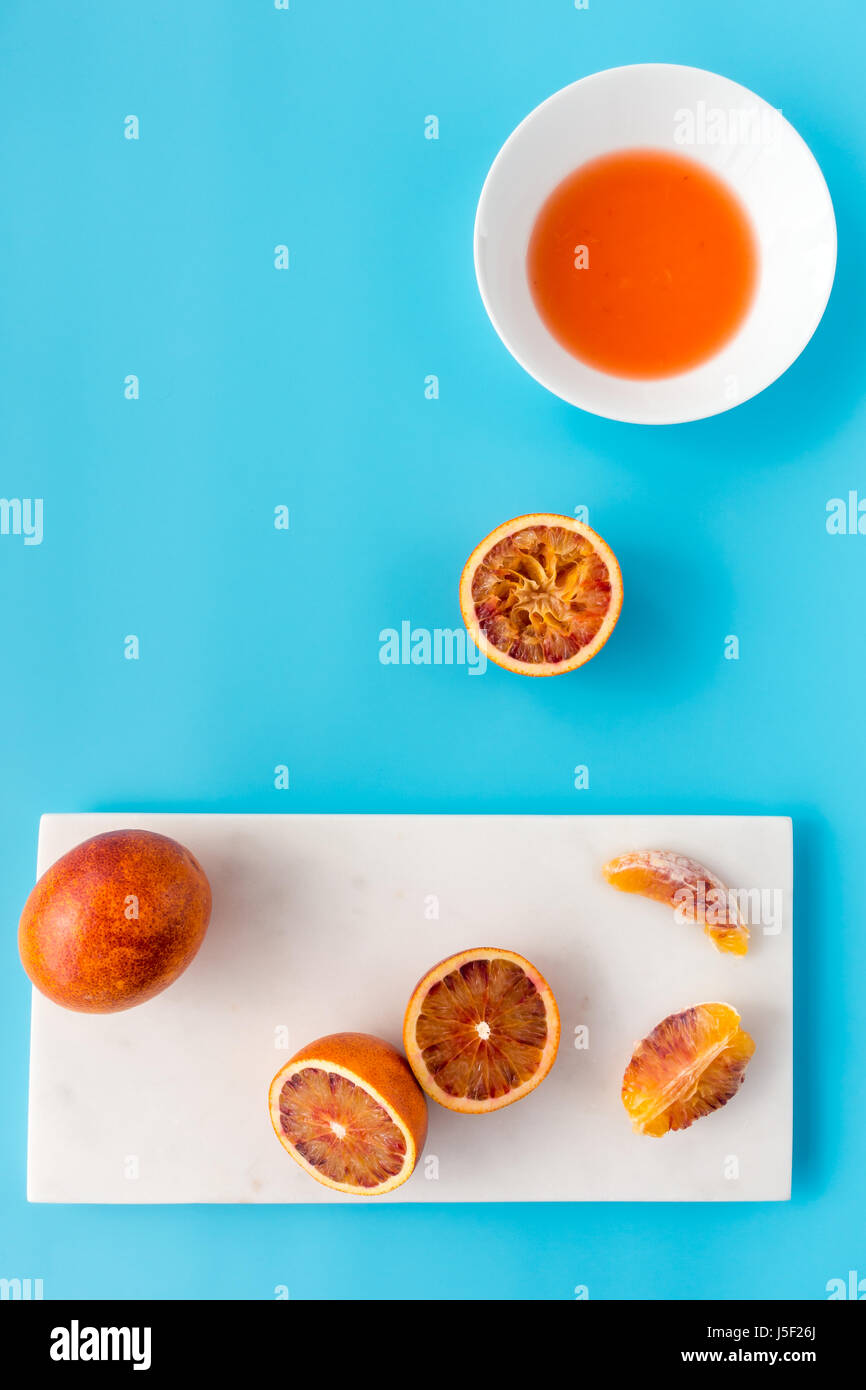 Tutto, dimezzata e spremuta di arance di sangue e succo di frutta fresco su marmo bianco tagliere e solido sfondo blu. Foto Stock