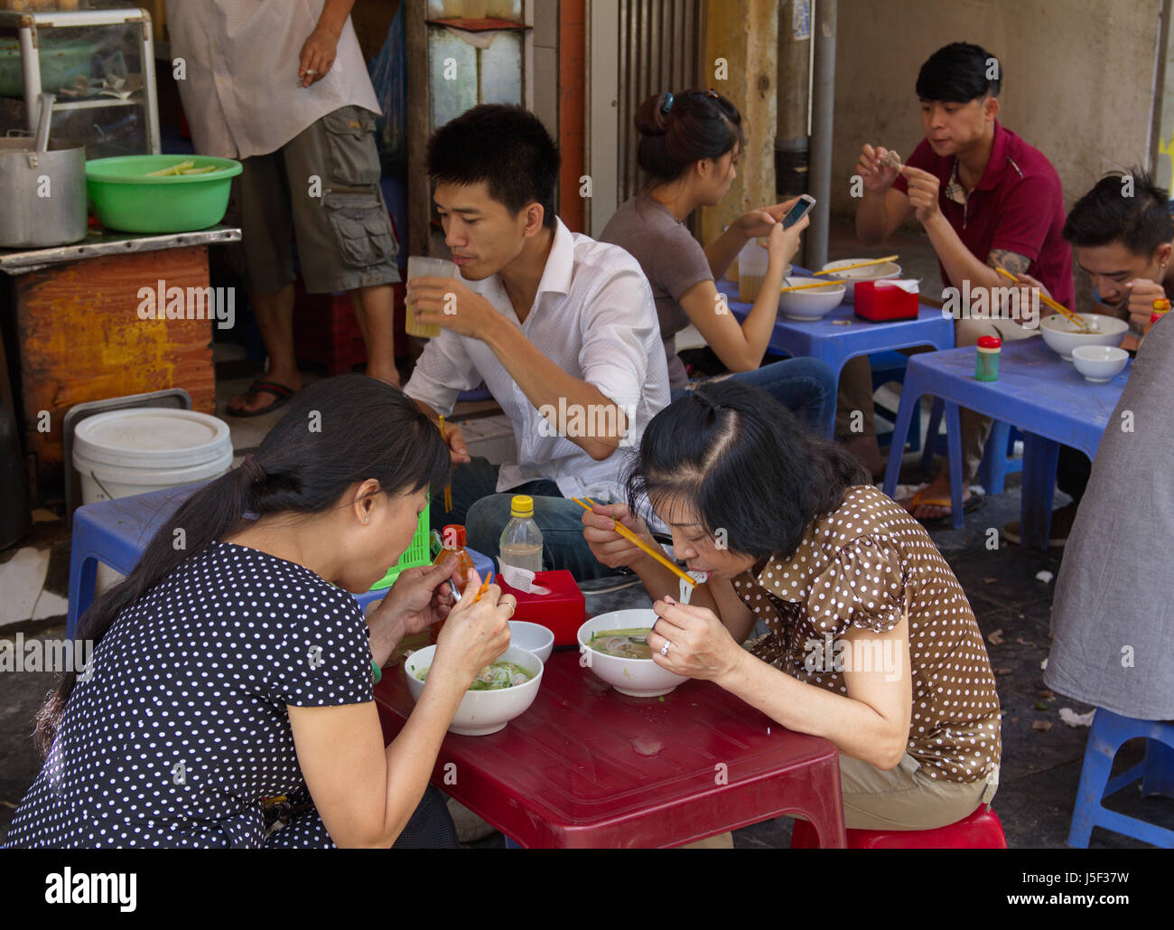 Persone mangiare tagliatelle al marciapiede tabelle nel vecchio quartiere, Hanoi, Vietnam Foto Stock