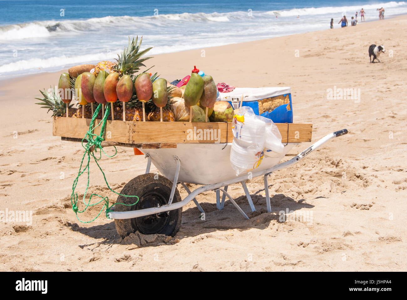 Una carriola in modo univoco e grossolanamente progettato per servire frutta e bevande presso una spiaggia, bella spiaggia, le persone e le onde in background Foto Stock