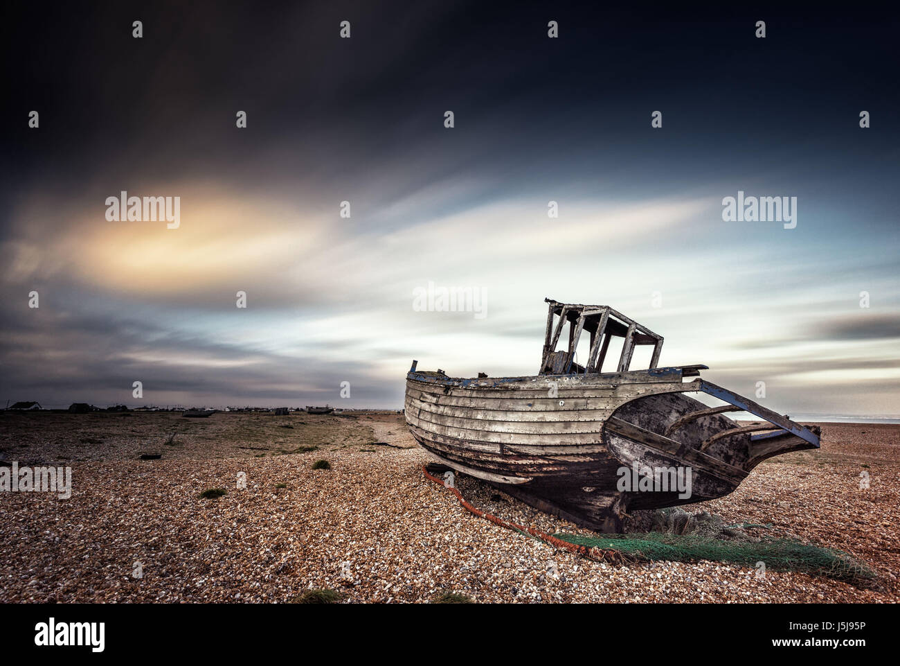 Singke abbandonato vecchia barca da pesca su una spiaggia di ciottoli con esposizione a lungo le nuvole. Dungeness, Inghilterra Foto Stock