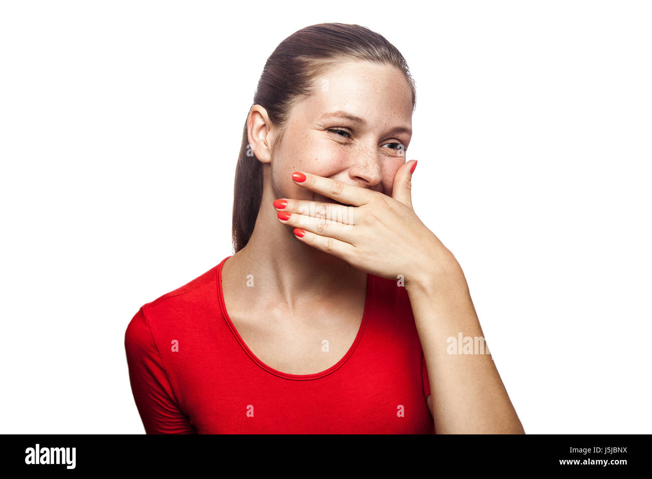 Ritratto di felice risate woman in red t-shirt con lentiggini con mano dietro la sua bocca. studio shot. isolato su sfondo bianco. Foto Stock
