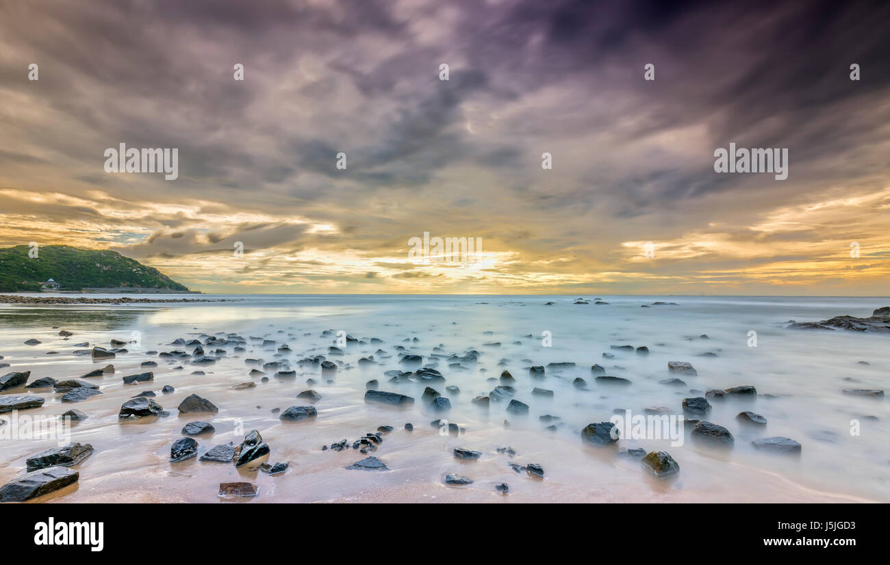 Alba sulla spiaggia con colorate nuvole, sotto una roccia con belle forme per creare bellissimi paesaggi benvenuti luminoso giorno freschi Foto Stock