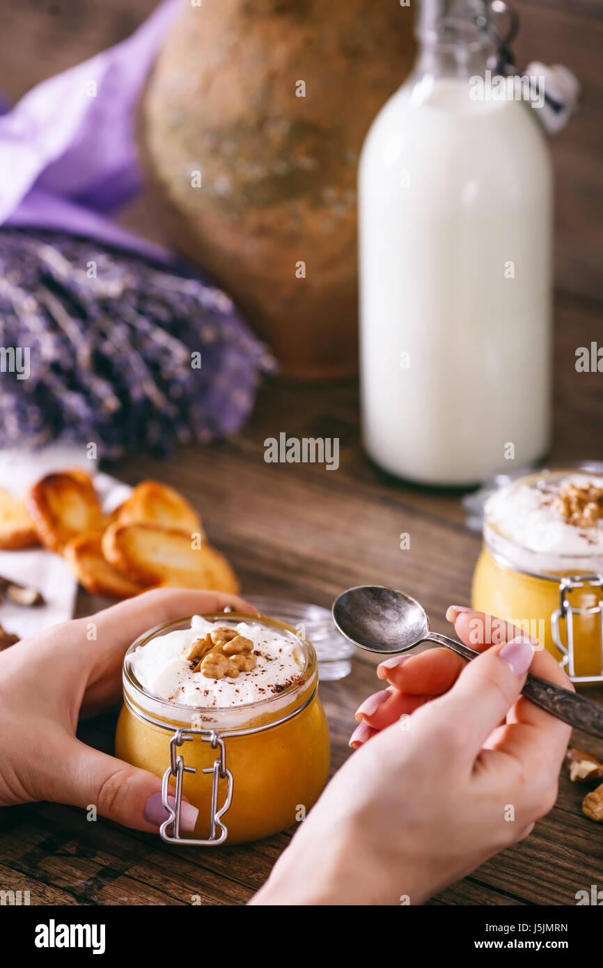 Le mani delle donne con il cucchiaio. Frullato di zucca in un barattolo di vetro con la panna montata, caramella mou, noce e miele biscotti. Bottiglia di latte. Legno scuro dello sfondo. il fuoco selettivo. Foto Stock