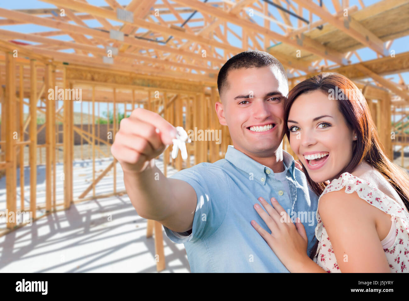 Giovane coppia militare sul sito con le chiavi di casa dentro la loro nuova casa Costruzione Framing. Foto Stock