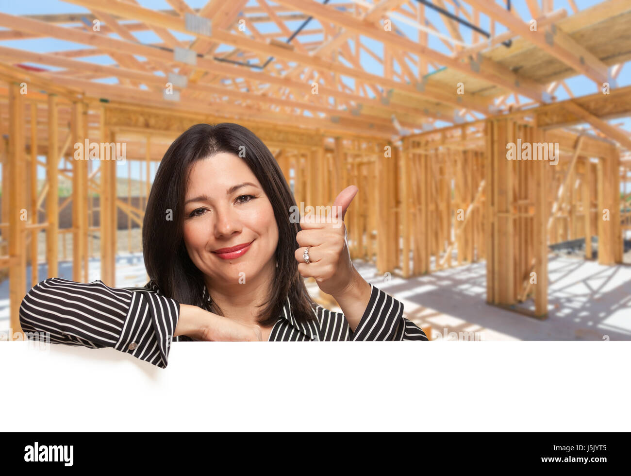 Donna ispanica con il pollice in alto sul sito all'interno di nuova costruzione in casa Framing. Foto Stock