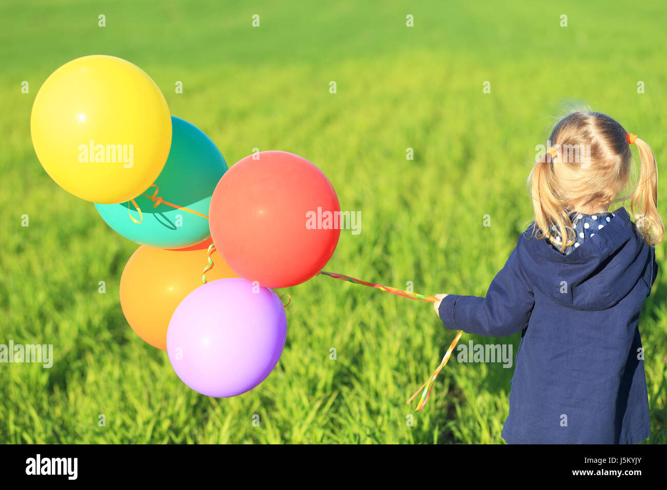 Una ragazzina con palloncini di close-up. Il capretto con palloncini colorati sul prato verde dello sfondo. Bambina con palloncini dal retro. Bambino libertà conc Foto Stock