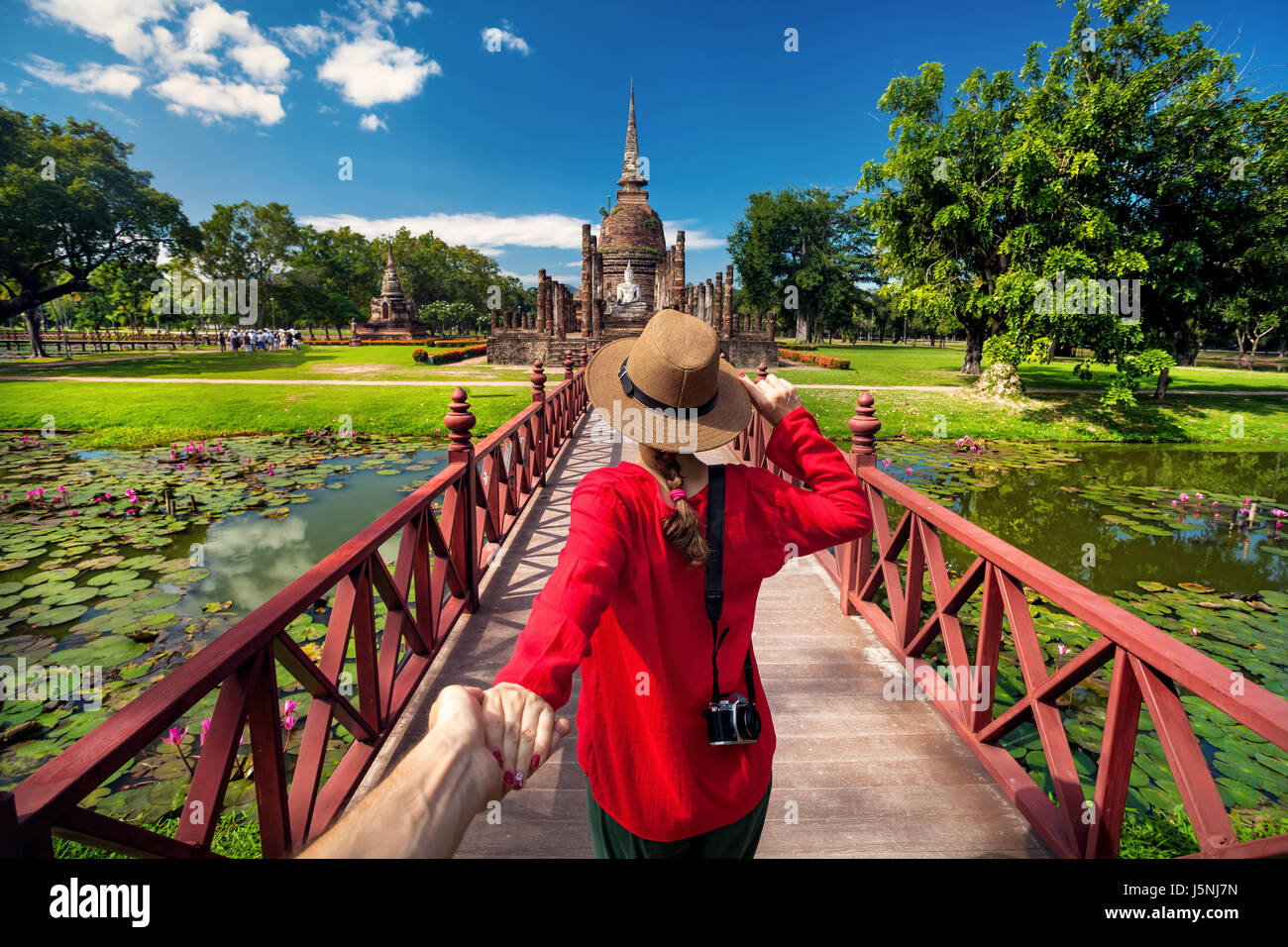 Donna turistica in maglietta rossa tenendo il marito a mano e andando a antico stupa in Sukhohai parco storico, Thailandia Foto Stock