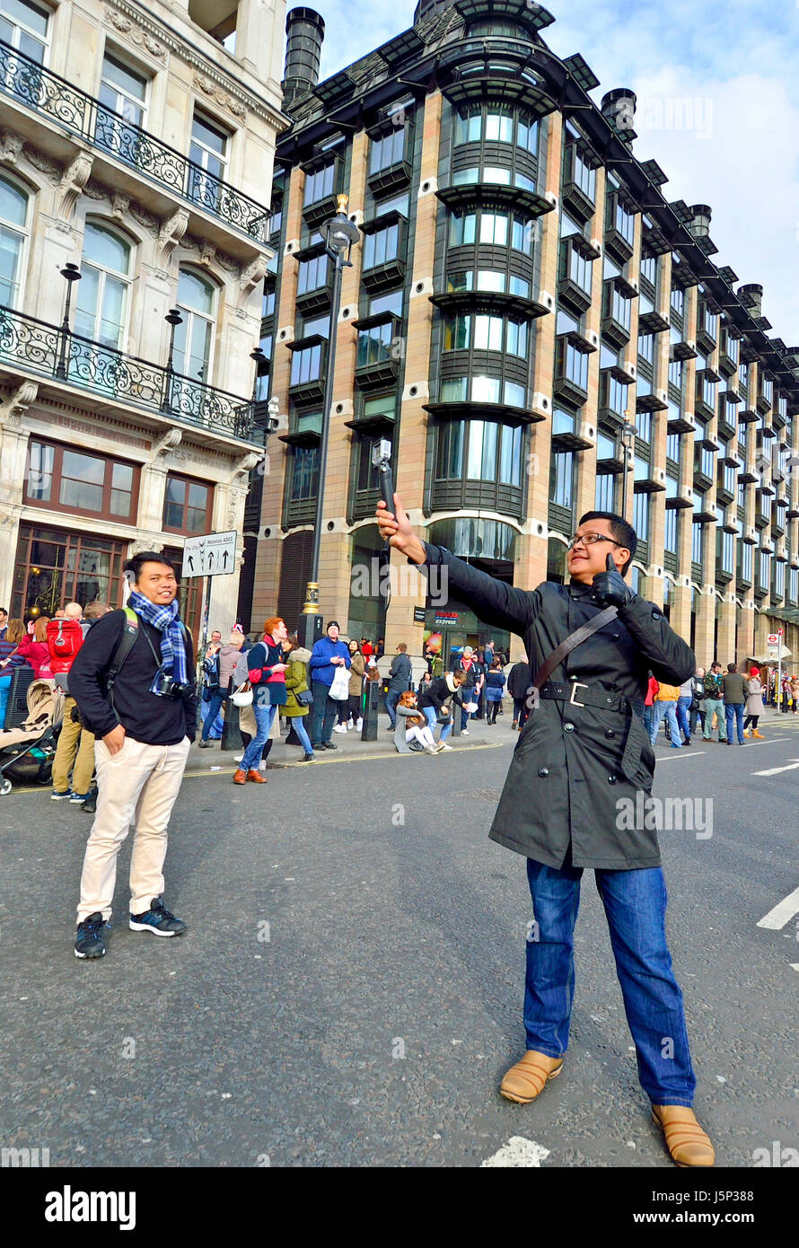 Londra, Inghilterra, Regno Unito. Asian turistica prendendo un selfie in piazza del Parlamento, Portcullis House (uffici parlamentari) dietro Foto Stock