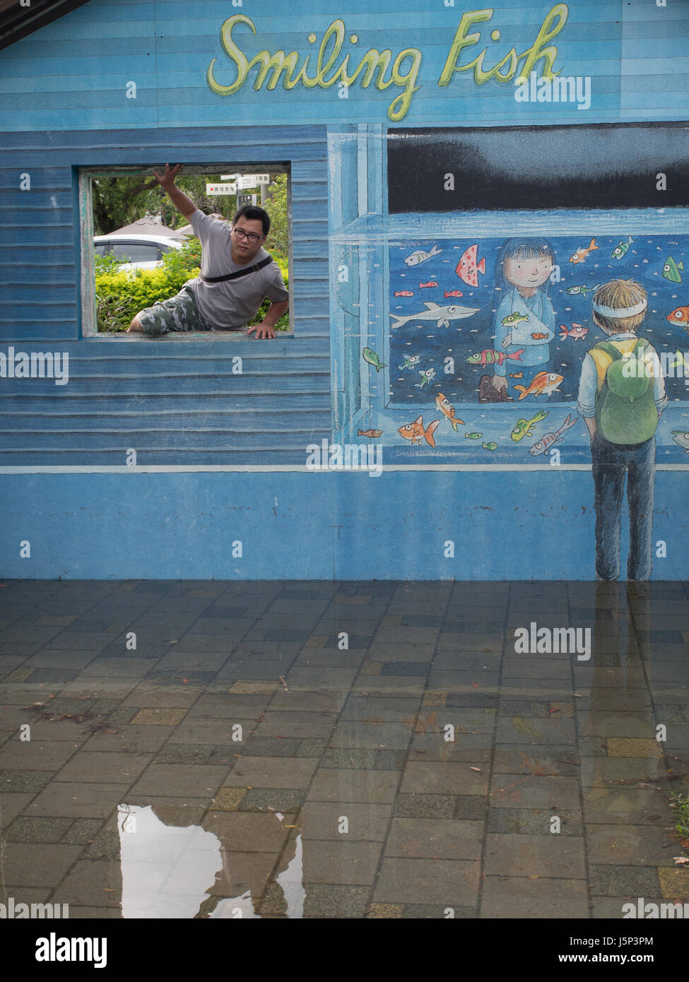 Yilan, Taiwan - 18 ottobre 2016:uomo Taiwanese passando attraverso una finestra / foro nella parete blu con disegni colorati Foto Stock