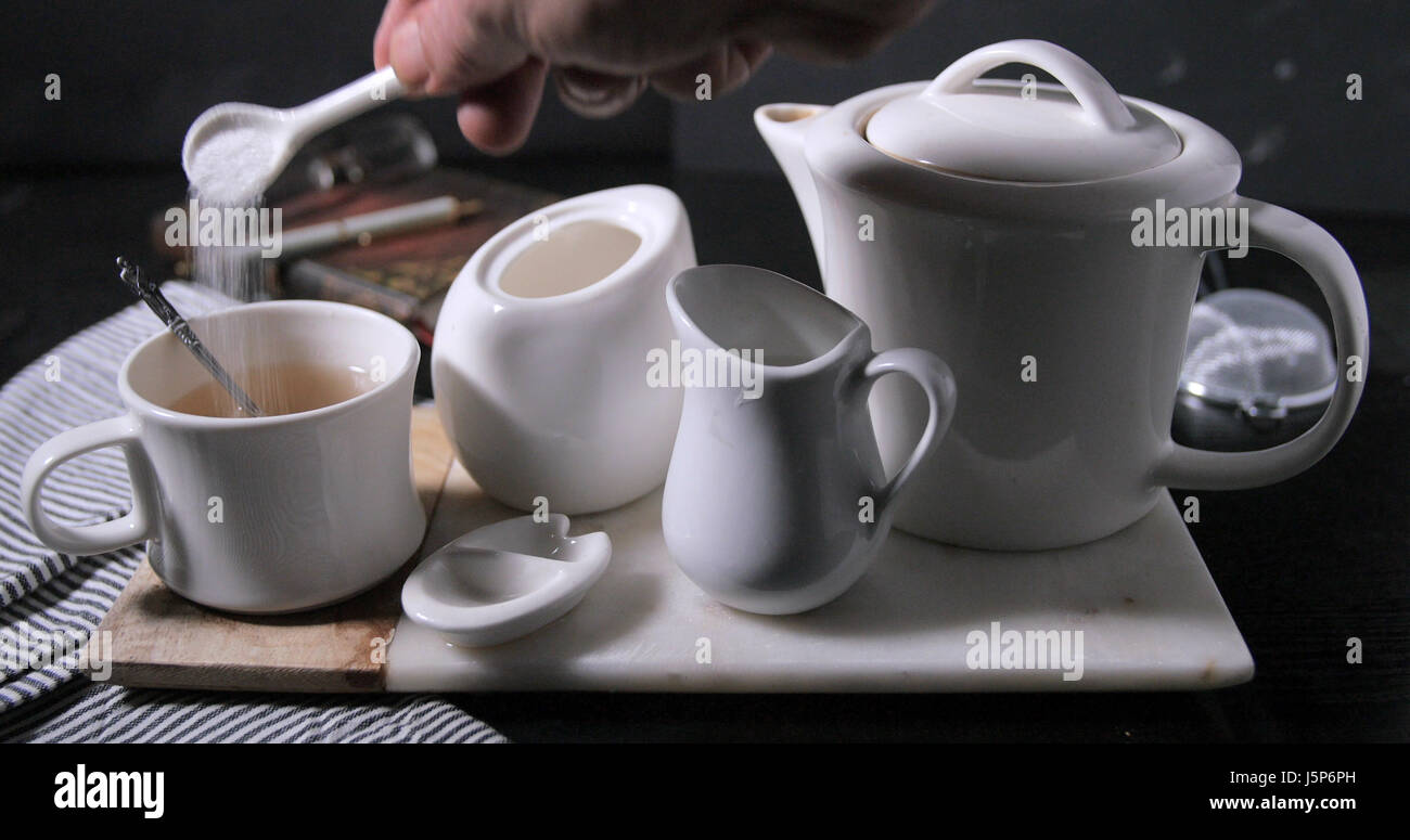 Aggiunta di zucchero per una bella calda fumante tazza di tè dal tè pentola Foto Stock