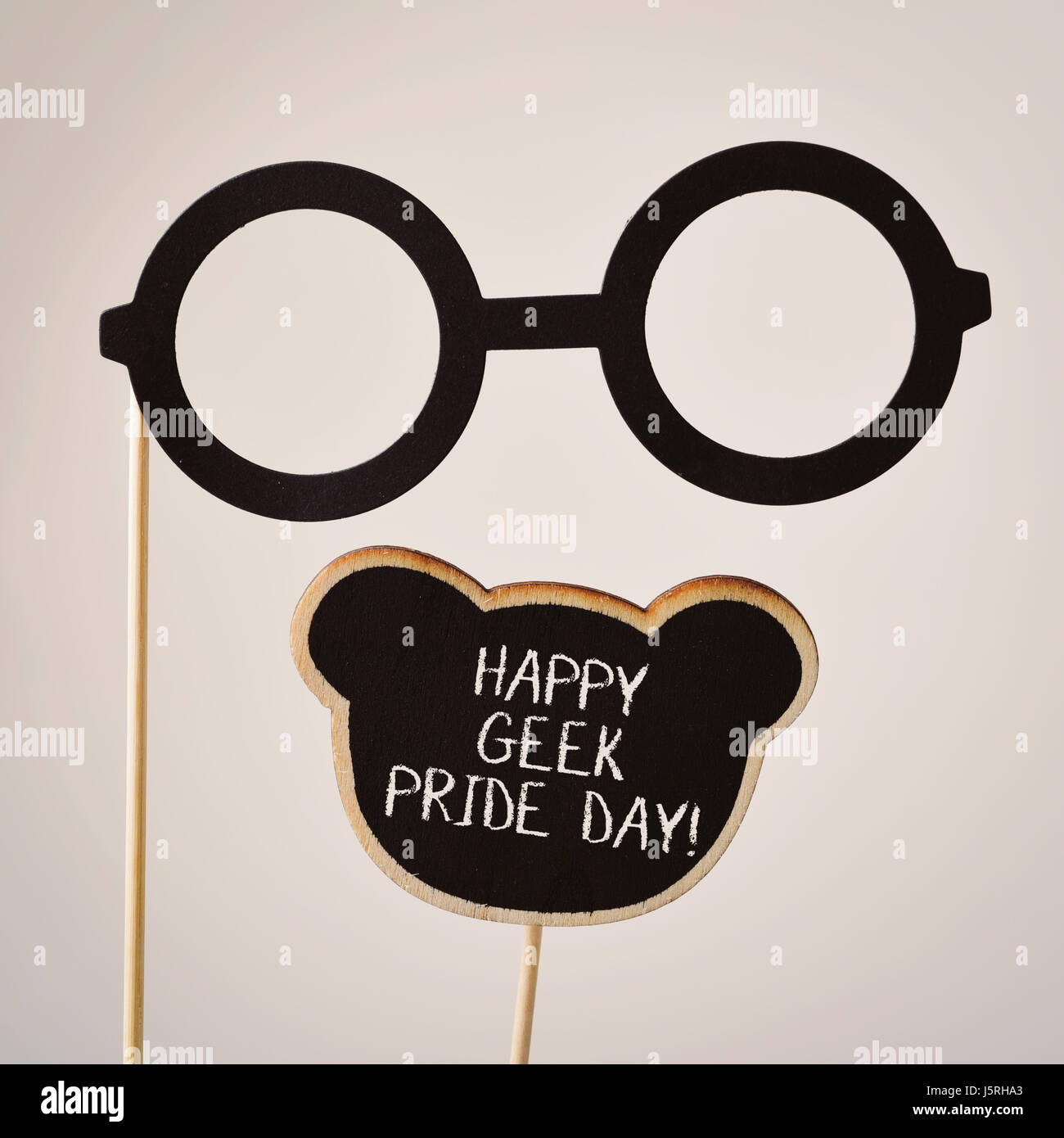 Una coppia di round-incorniciato occhiali attaccata a un manico in legno e il testo happy geek pride scritto in un cartello nero, su un fondo bianco Foto Stock