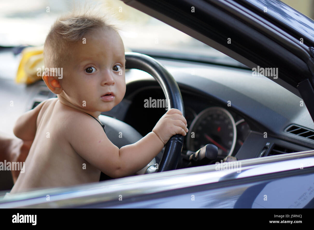 Carino piccolo autista ragazzo seduto in macchina e mantiene la ruota. La primavera. Foto Stock