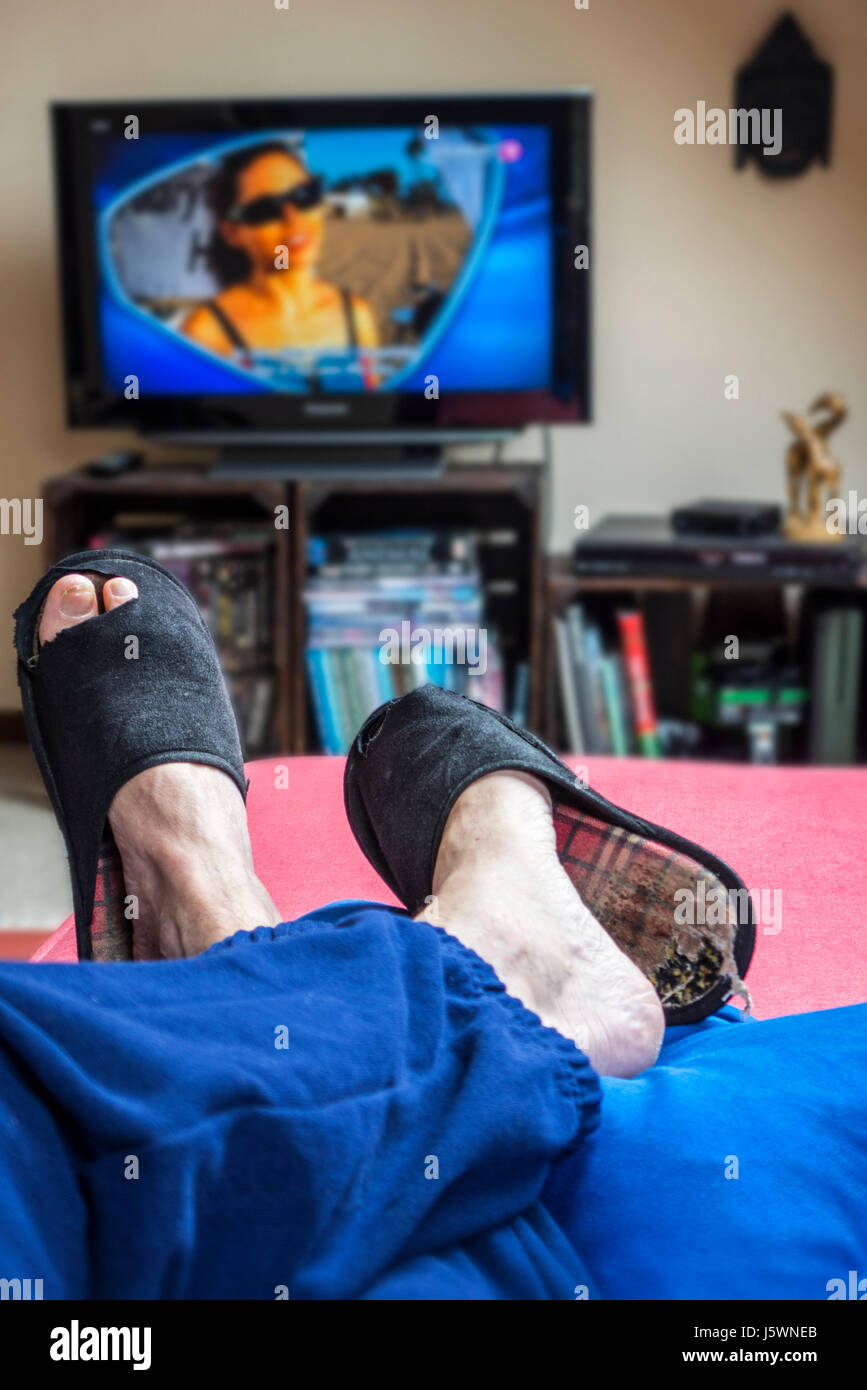 Couch Potato, pigro nella comoda poltrona indossando indossato pantofole con grande dita tramite incollaggio e guardare la televisione in salotto Foto Stock