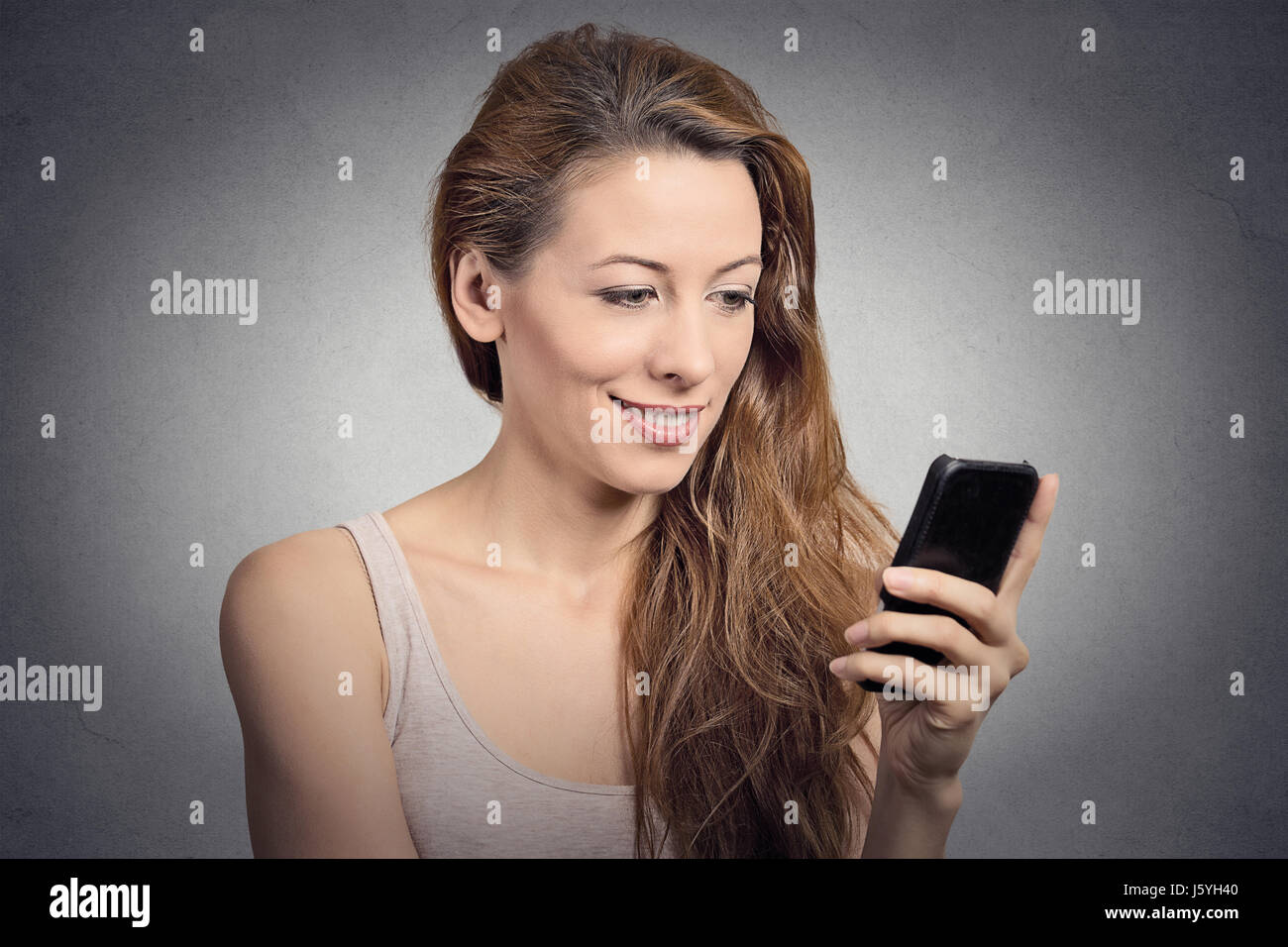 Ritratto felice, donna sorridente texting utilizzando smart phone isolato muro grigio Sfondo. Concetto di comunicazione. Positive le espressioni facciali di emozione sentire Foto Stock