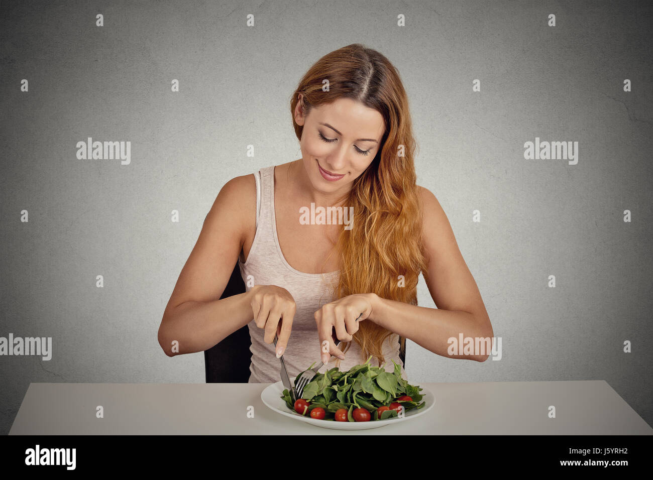 Ritratto sorride attraente giovane donna mangiare insalata verde isolato sul muro grigio Sfondo studio shot. sani e freschi dieta alimentare il concetto di nutrizione Foto Stock