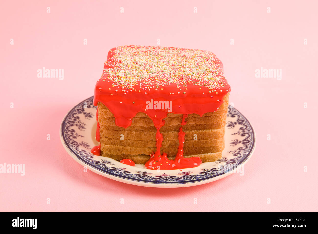 Un eccentrico ciliegina compleanno pane ricoperte con un pizzico di colore rosso e il coulis su sfondo rosa Foto Stock