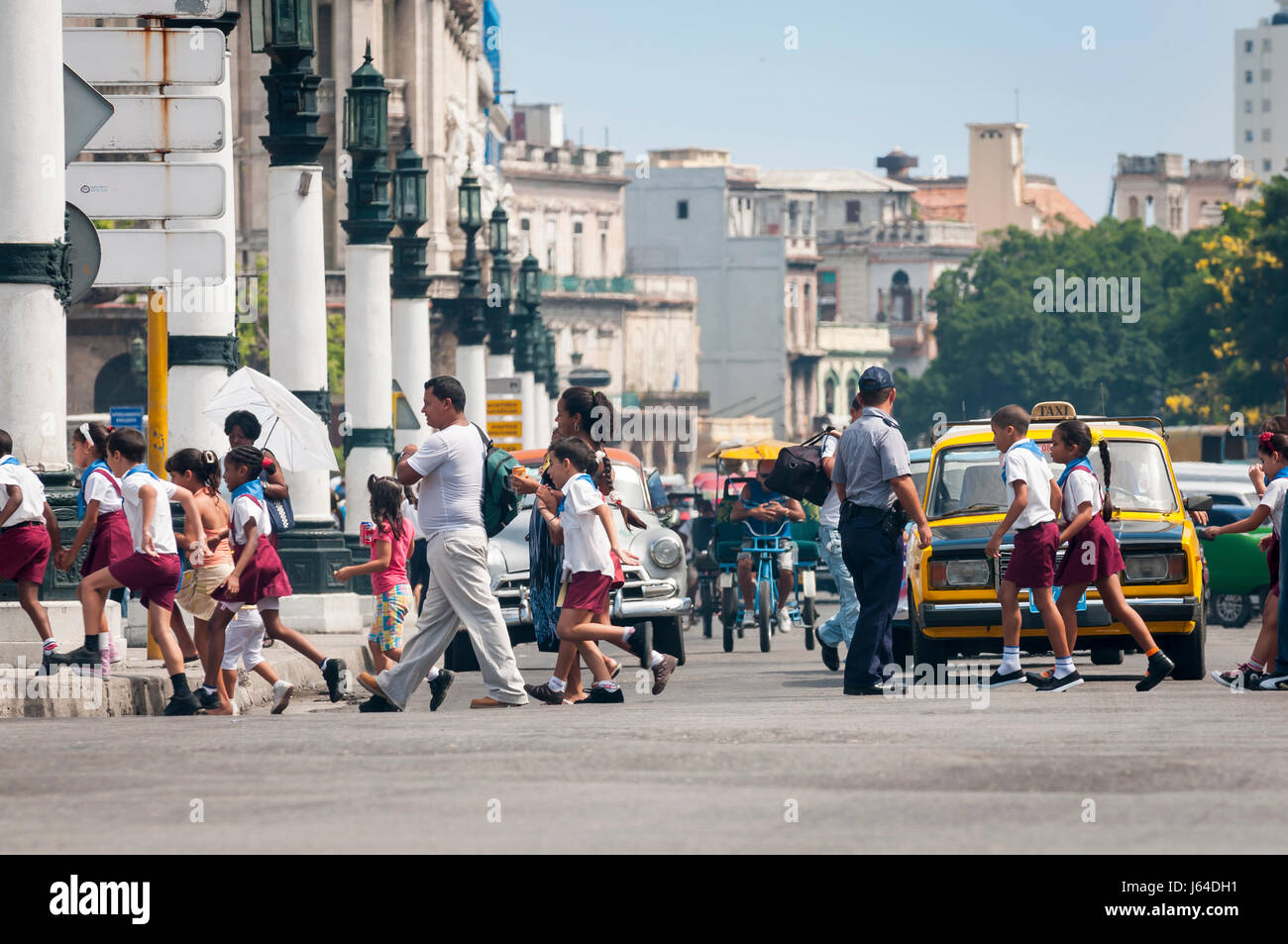 L'Avana - circa giugno, 2011: un gruppo di scuola cubana di bambini in uniforme di attraversare la strada di fronte ad un tipico lineup del vecchio russo e auto americane. Foto Stock