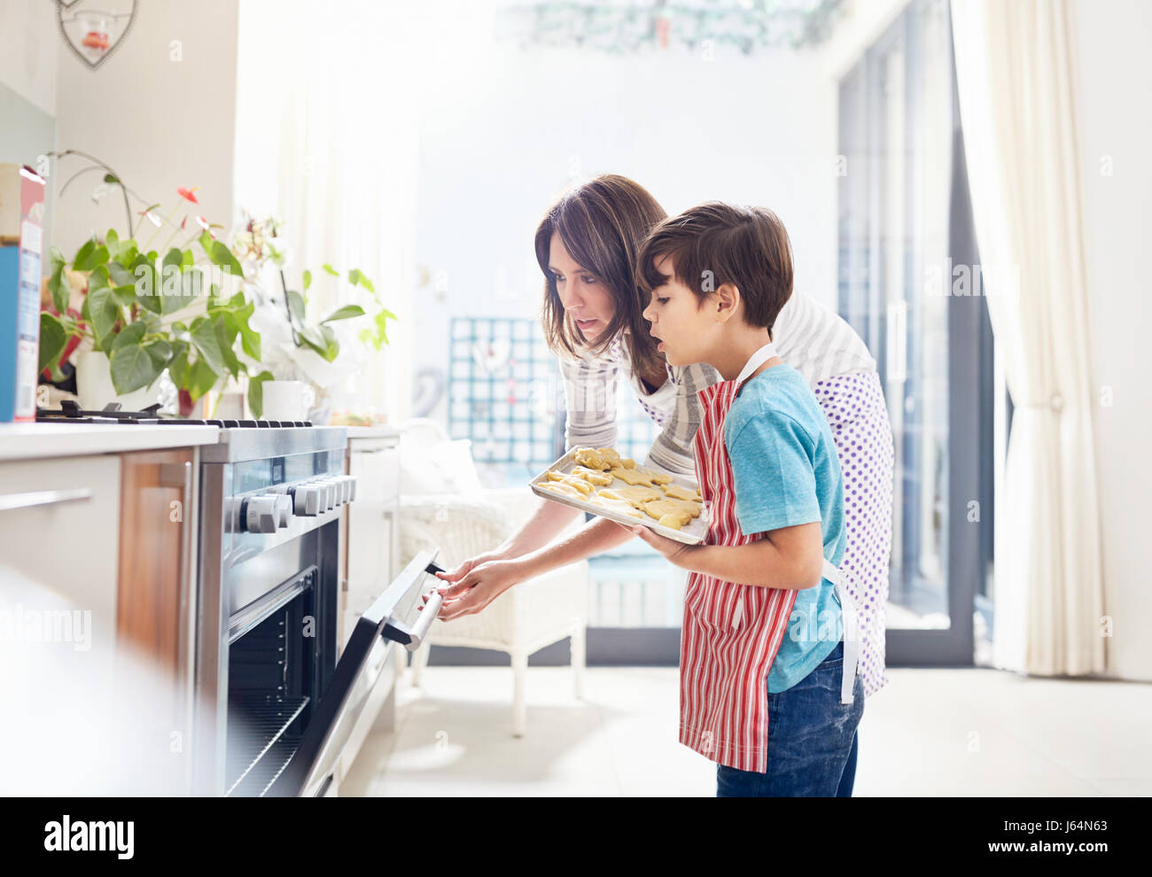 Madre e figlio di cottura in forno, posizionando i cookie nel forno in cucina Foto Stock