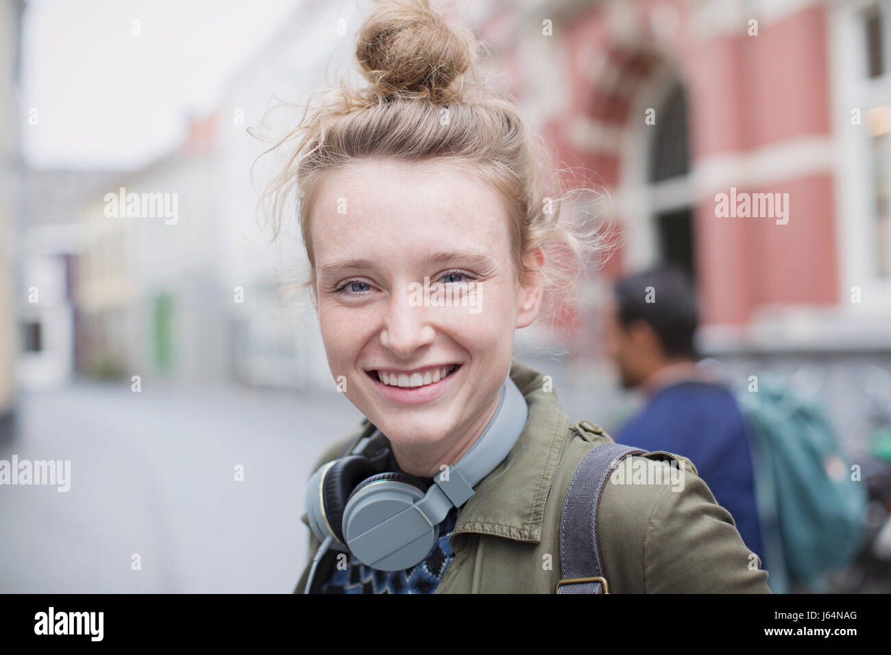 Ritratto sorridente giovane donna con le cuffie sulla strada di città Foto Stock