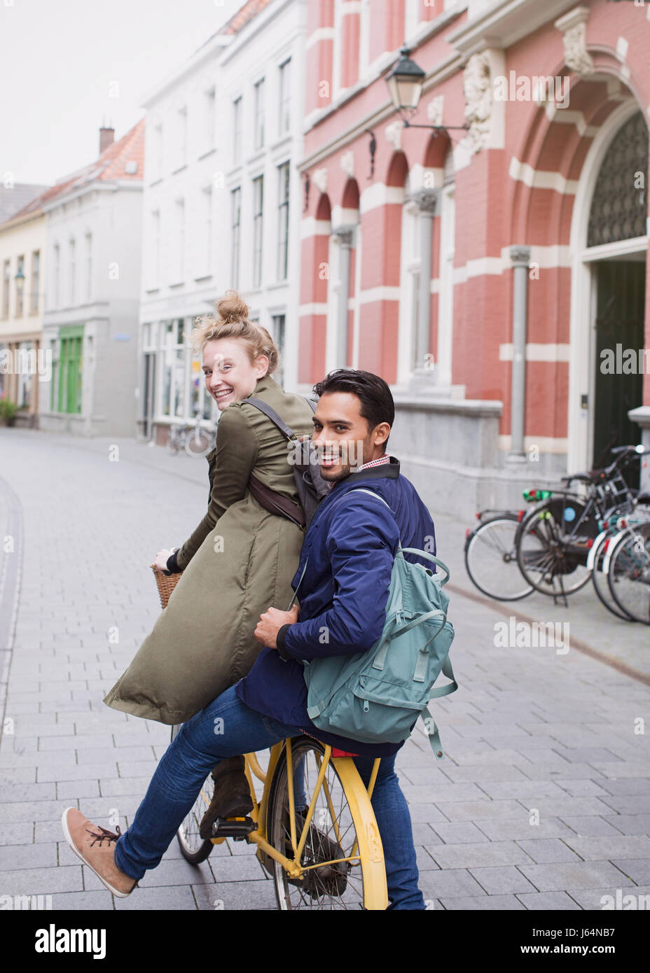 Ritratto sorridente giovane uomo e donna Bicicletta Equitazione sulla strada di città Foto Stock