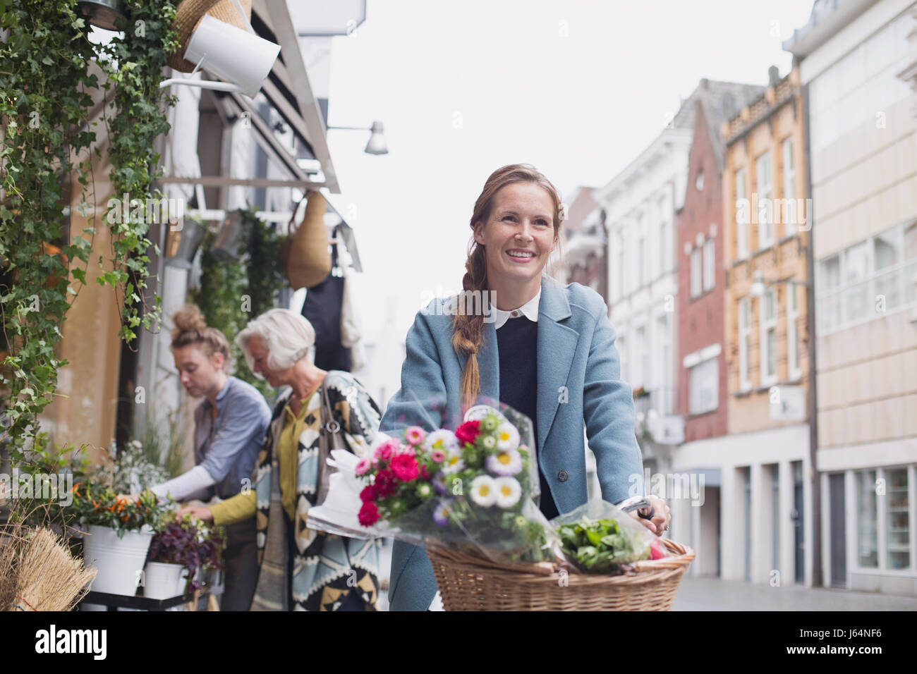 Donna sorridente equitazione Bicicletta con fiori in cesto su strada di città Foto Stock