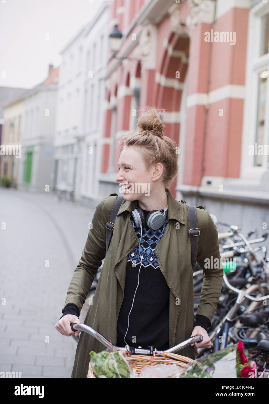 Sorridente giovane donna con cuffie equitazione Bicicletta su una strada di città Foto Stock