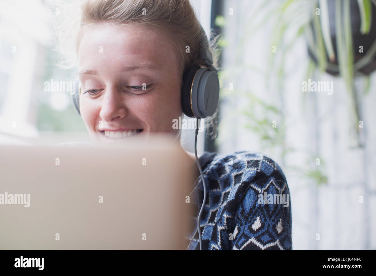 Sorridente giovane donna con cuffie utilizzando laptop in cafe Foto Stock