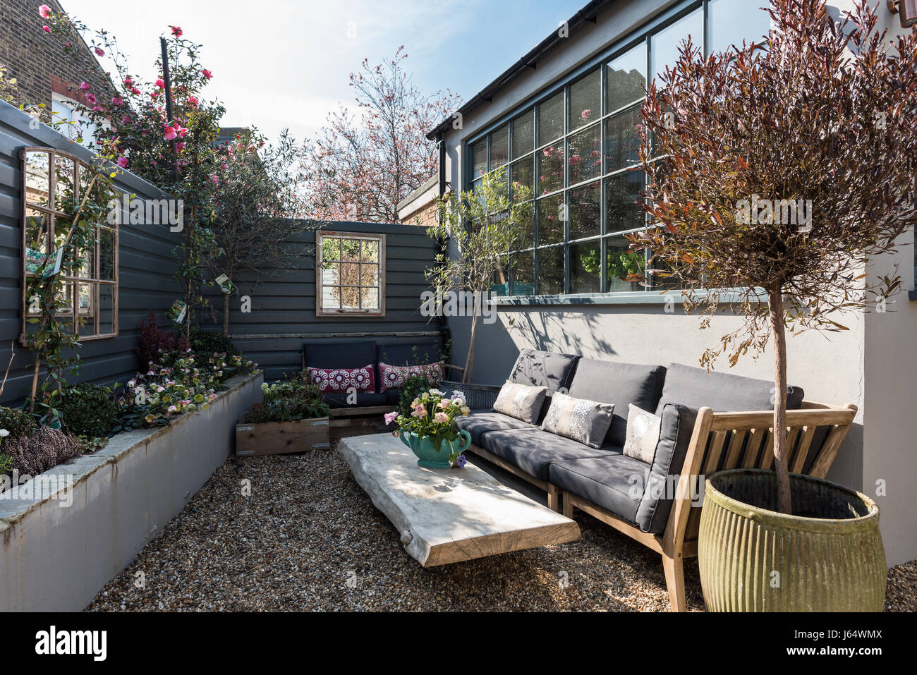 Accogliente cortile giardino con vetri a specchio e un divano. Il cladding shiplap è dipinto nella parte iniziale da Farrow & Ball Foto Stock