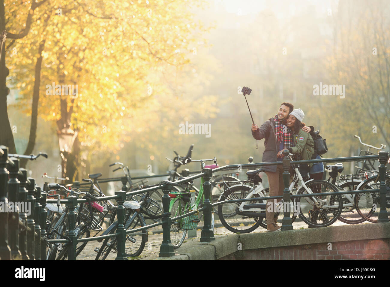 Coppia giovane con le biciclette tenendo selfie con selfie stick sul ponte autunno, Amsterdam Foto Stock