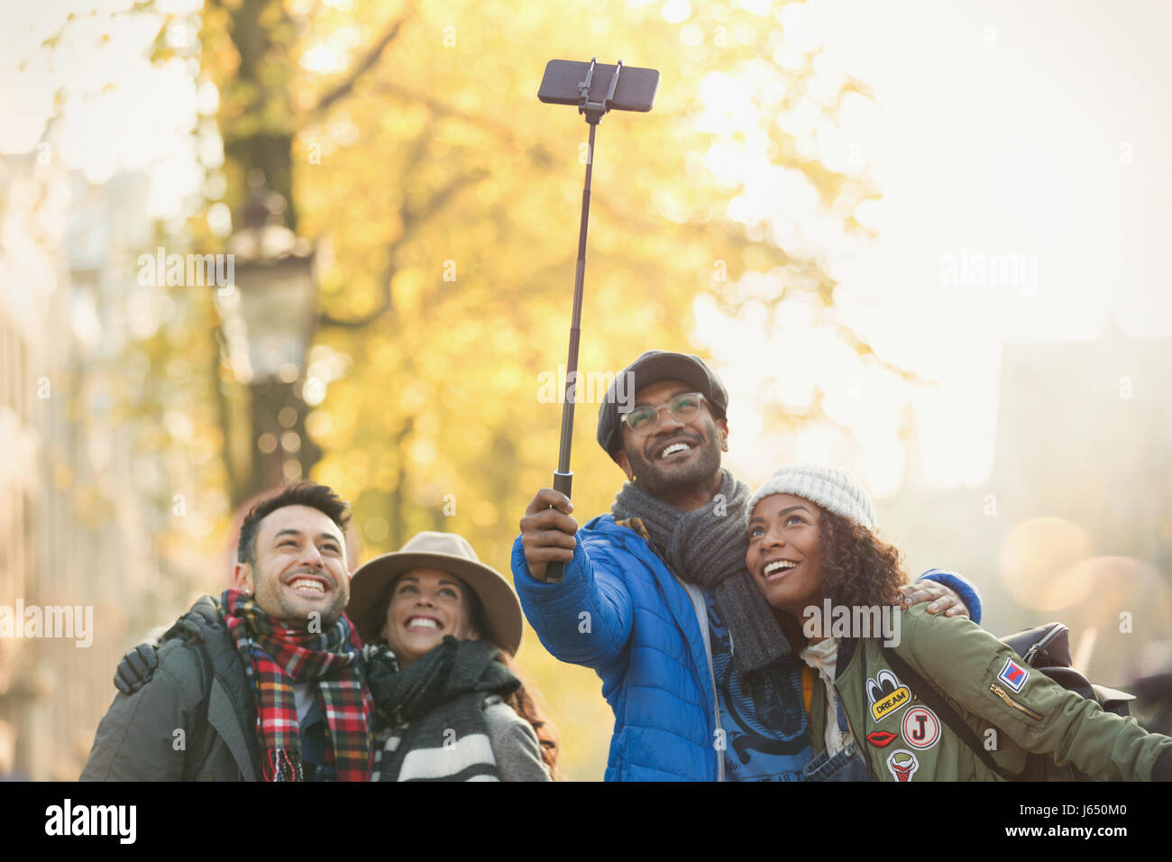Sorridente coppia giovane amici prendendo selfie con selfie stick sulla strada di autunno Foto Stock