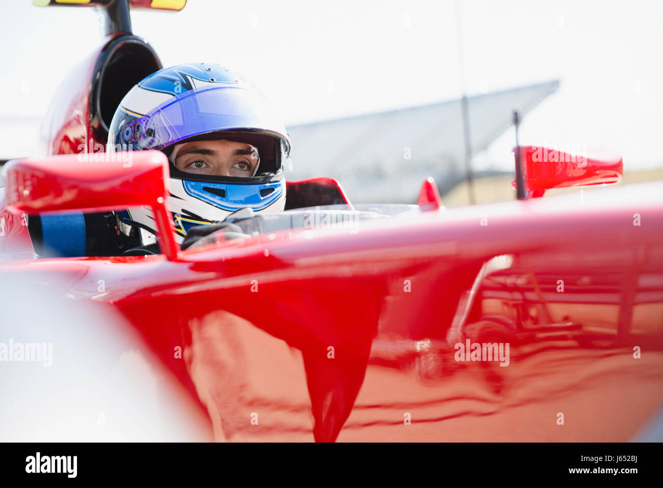 Focalizzato gara di Formula Uno pilota di auto che indossa il casco, guardando lontano Foto Stock