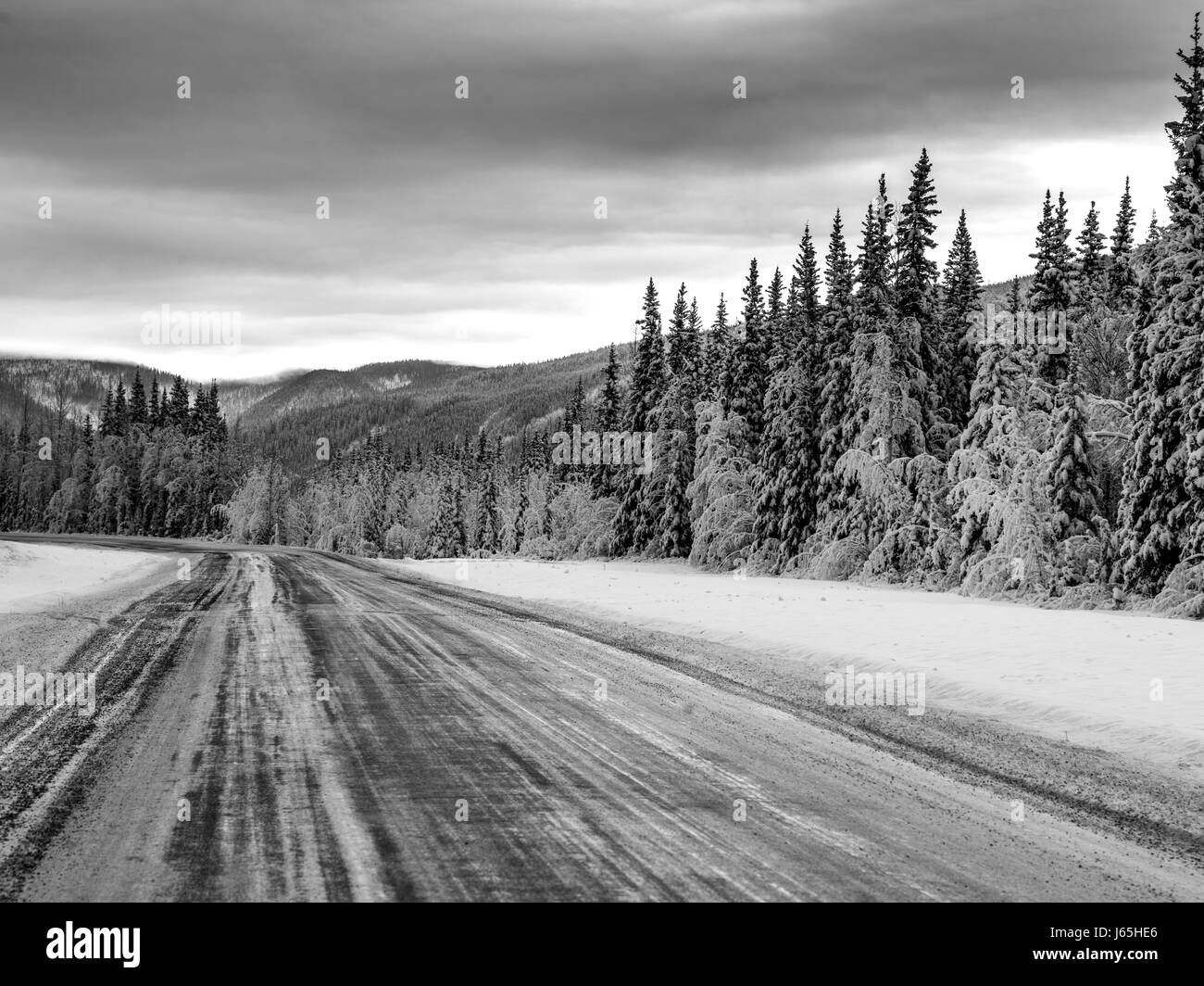 Autostrada passando attraverso la coperta di neve la foresta, Alaska Highway, Northern Rockies municipalità regionale, British Columbia, Canada Foto Stock