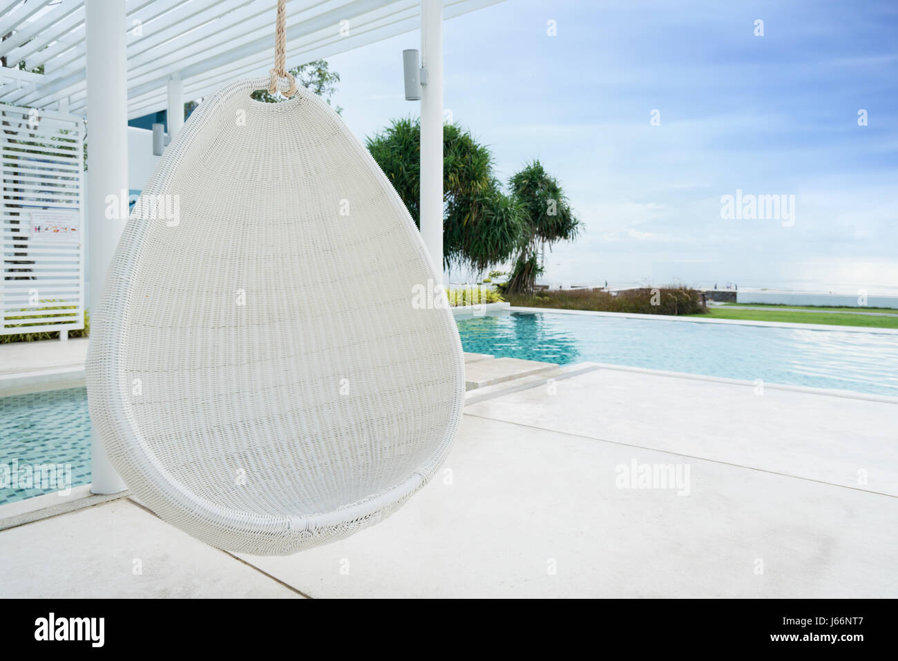 Rilassante white rattan sedia pensili a piscina sul mare per vacanza, estate e concetto di viaggio. Foto Stock