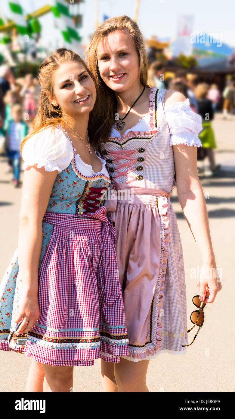 Due attraenti donne giovani al parco di divertimenti tedesco Oktoberfest con tradizionale Dirndl vestiti e Merry Go Round in background Foto Stock