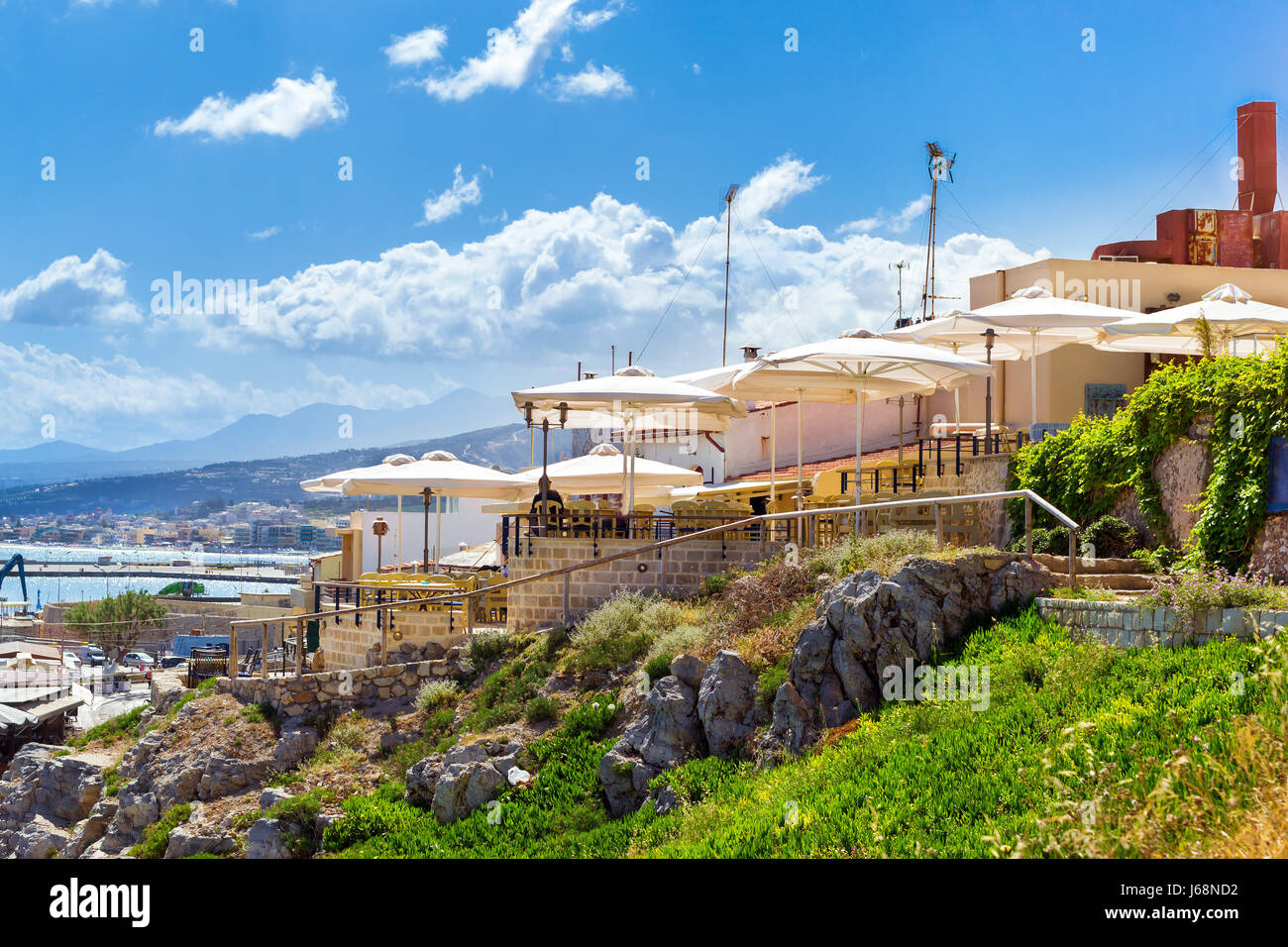 Resort Outdoor cafe con ombrelloni bianchi sulla sommità di una collina sopra l'autostrada lungo la promenade Emmanouil Kefalogianni. Architettura greca sulla costa di Kolpos Alm Foto Stock
