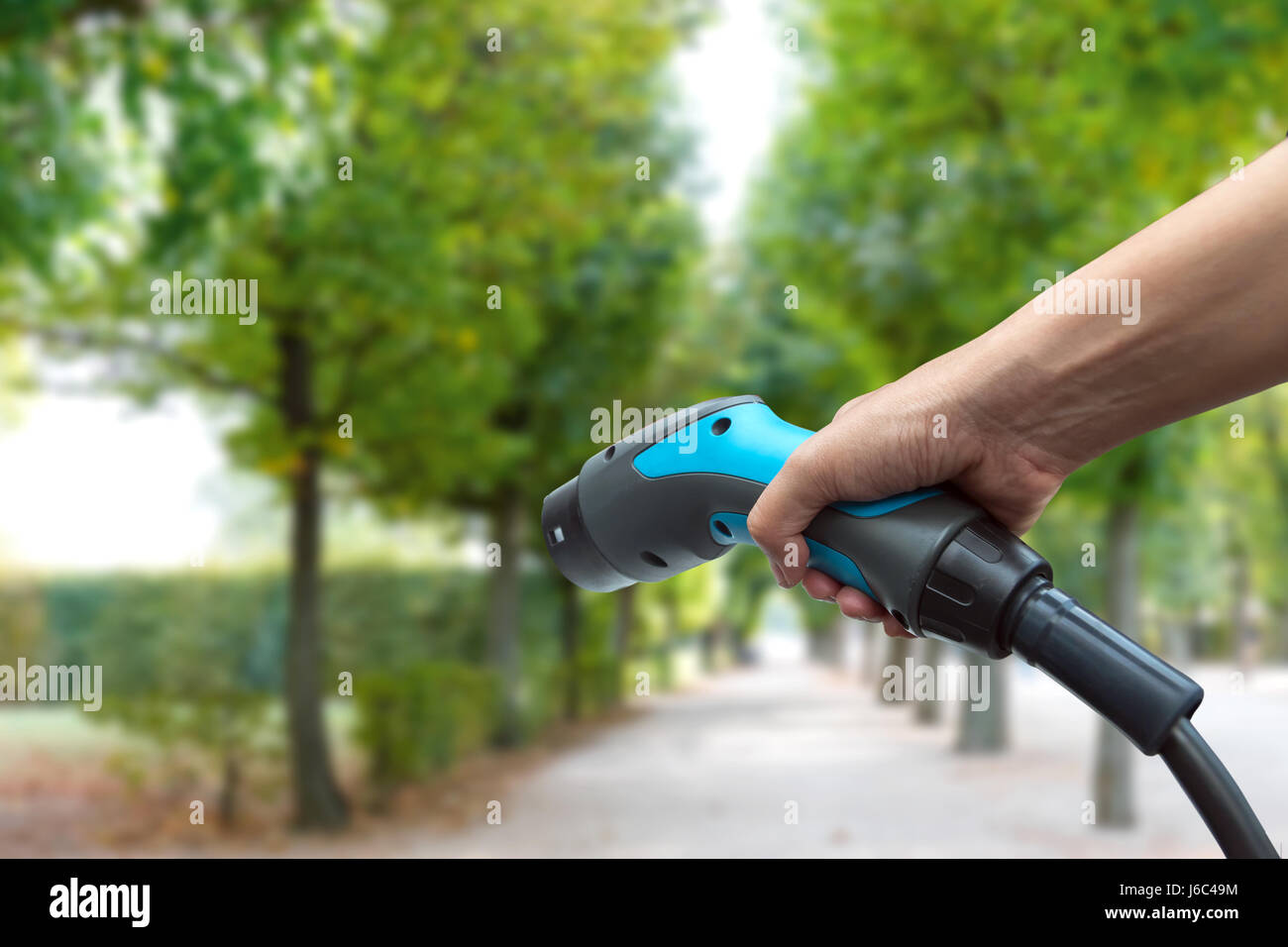 Inquinamento atmosferico e ridurre le emissioni di gas a effetto serra del concetto. Mano che mantiene e ricarica auto elettrica con il verde giardino naturale visualizzare lo sfondo. Foto Stock