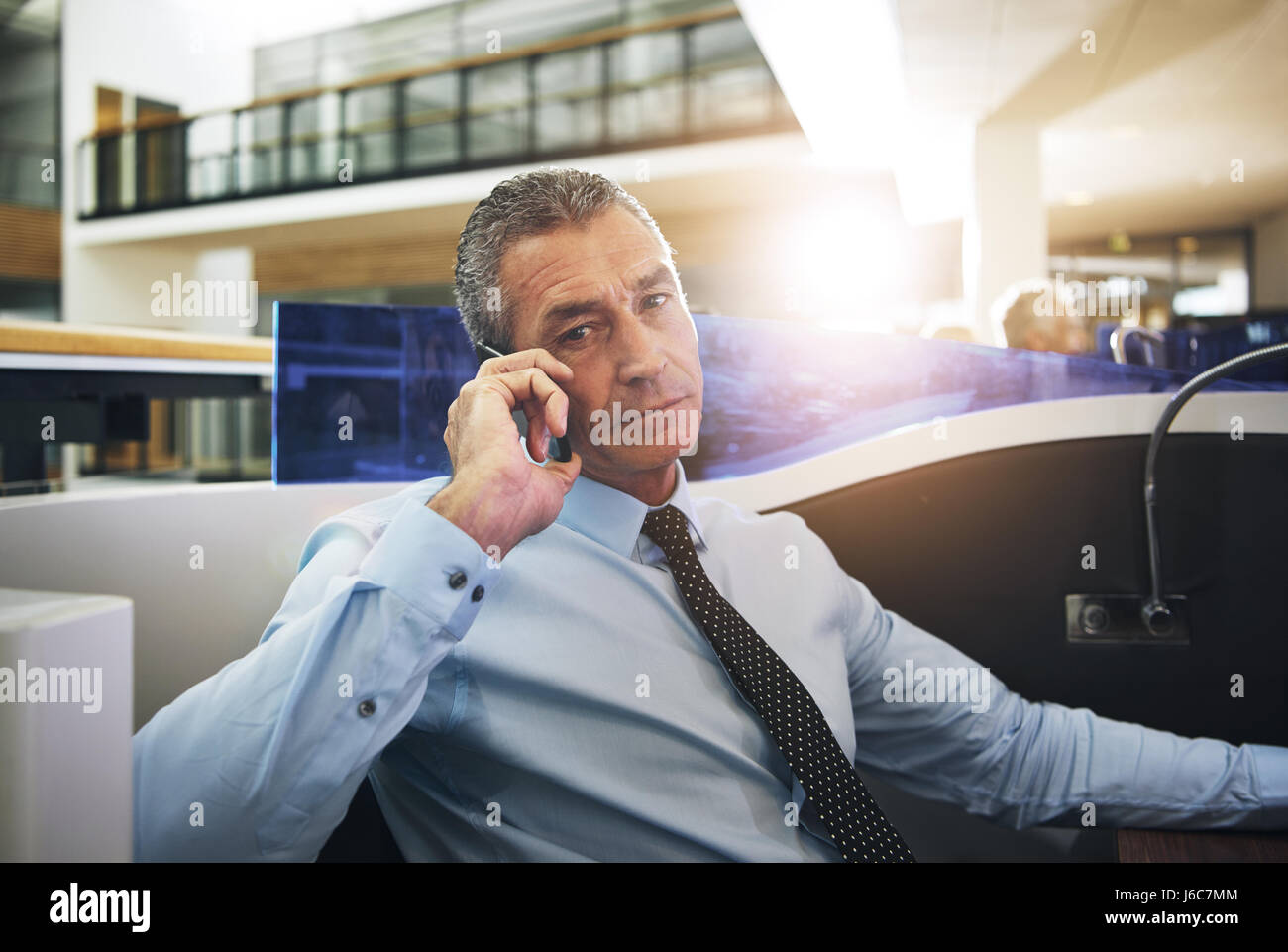 Fiducioso imprenditore maturo seduto e pensare in ufficio mentre avente conversazione telefonica. Foto Stock