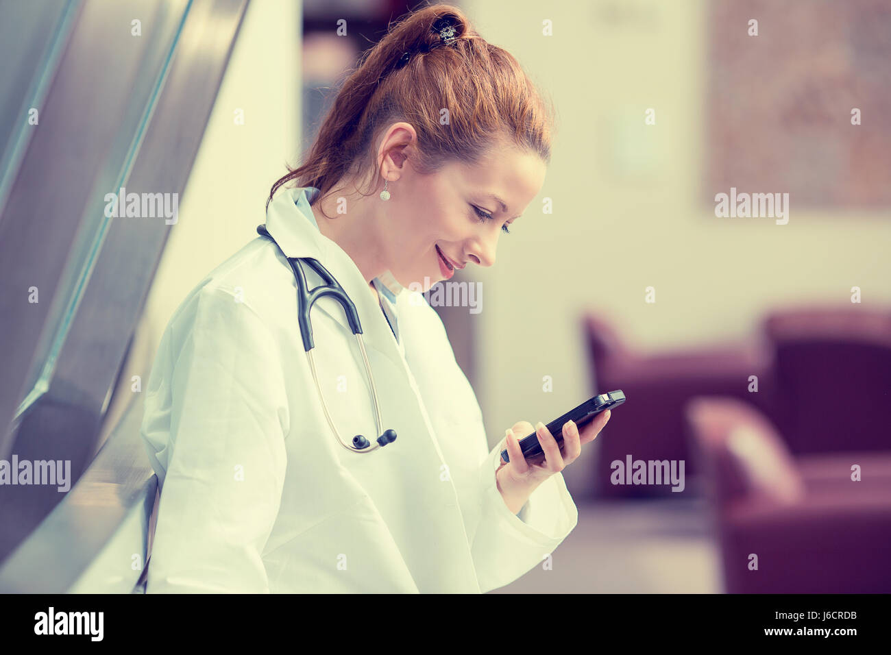 Profilo laterale ritratto femminile sorridente medico, professionista del healthcare in bianco camice con stetoscopio, analizzando i dati risultati su mobile smart phone Foto Stock