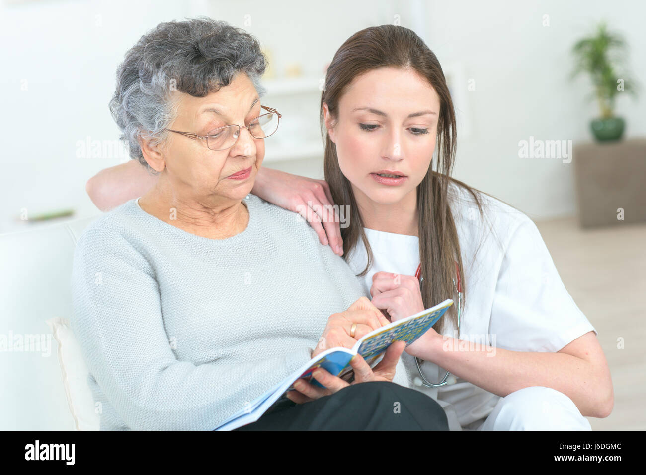 Signora anziana leggendo una rivista, più giovane donna dal suo lato Foto Stock