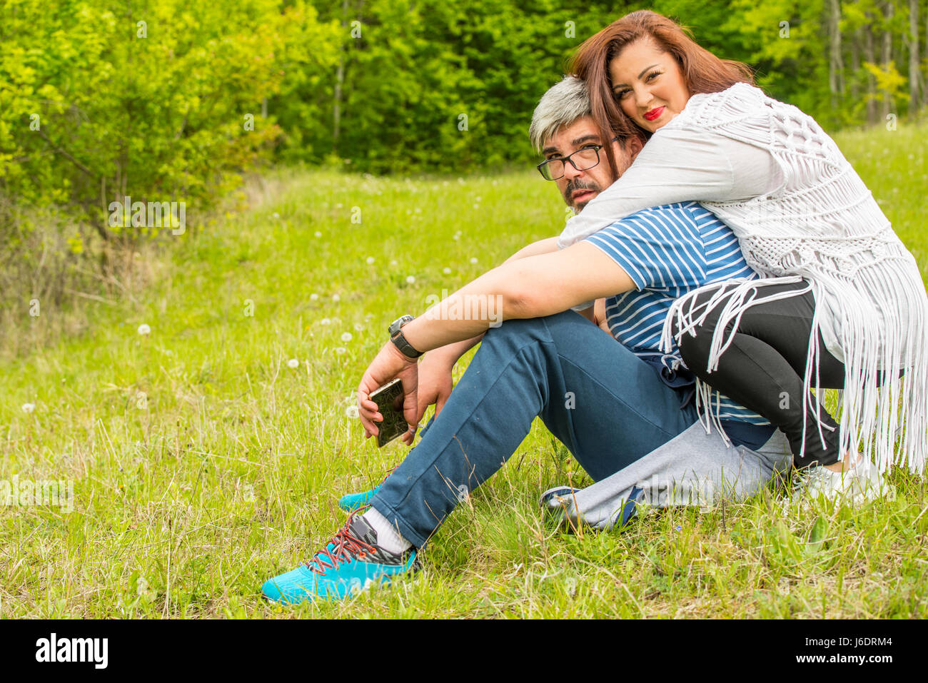 Felice coppia seduta in erba di abbracciare insieme Foto Stock