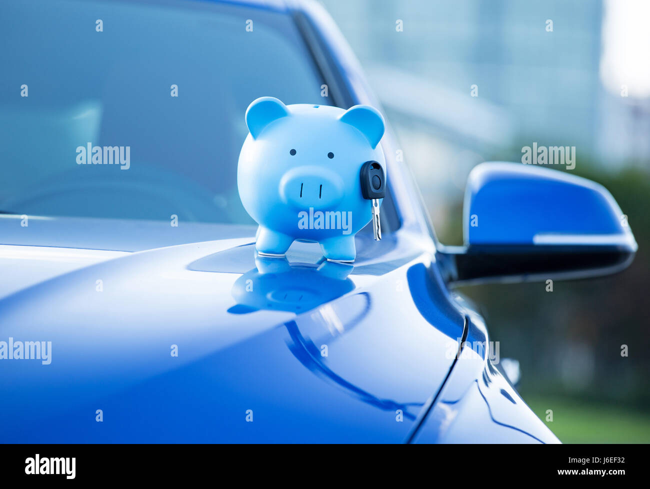 Primo piano immagine ritagliata blue nuova vettura con il salvadanaio e la chiave sul cofano, isolato al di fuori di edifici aziendali. Concessionaria che offre la linea di credito finanziare servi Foto Stock