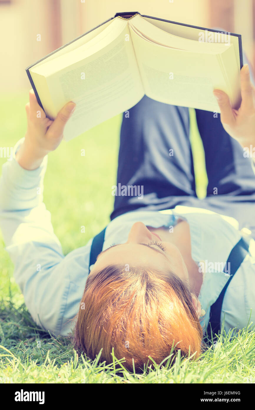 Studente nel parco. Gioiosa felice ragazza giovane studente seduto libro di lettura esterno sul campus universitario o di parcheggio. Il concetto di istruzione. Volto positivo Foto Stock