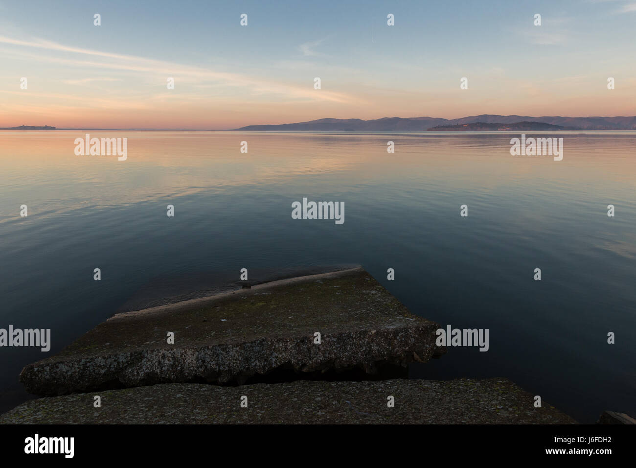 Un semi-sommersa molo di cemento su un lago, al tramonto, con belle morbidi e caldi colori e riflessi Foto Stock
