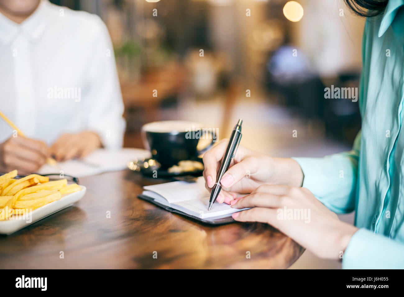 Due donne iscritto nelle loro note in un coffee shop Foto Stock