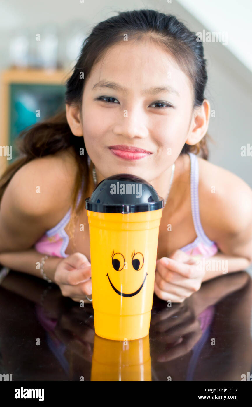 Attraente giovane donna asiatica con novità smiley tazza in plastica in una impostazione di interni Foto Stock