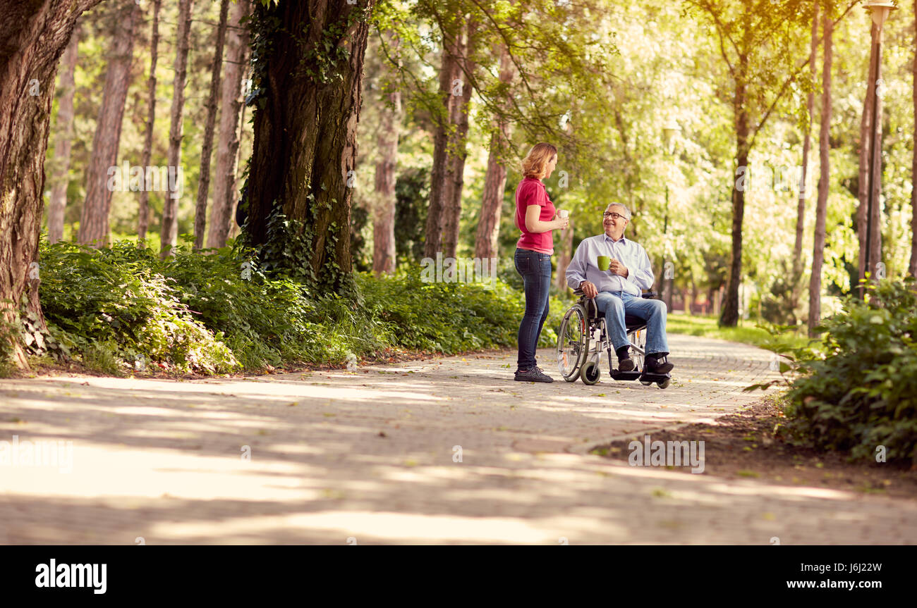 Donna sorridente con il suo disabili padre felice in carrozzella godendo il tempo insieme all'aperto Foto Stock